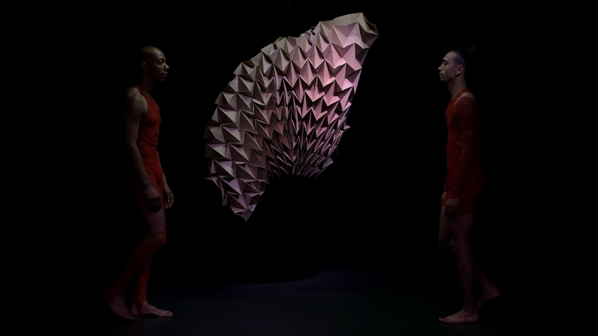 Shamel Pitts and Tushrik Fredericks facing each other across the stage, the folded paper sculpture between them.
